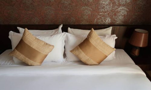 Stock photo showing a luxury double king size bed, which looks opulent with its clever use of colour, wooden headboard against the wall and matching golden scatter cushions, home furnishings and bedroom interior design with gold pattern design.